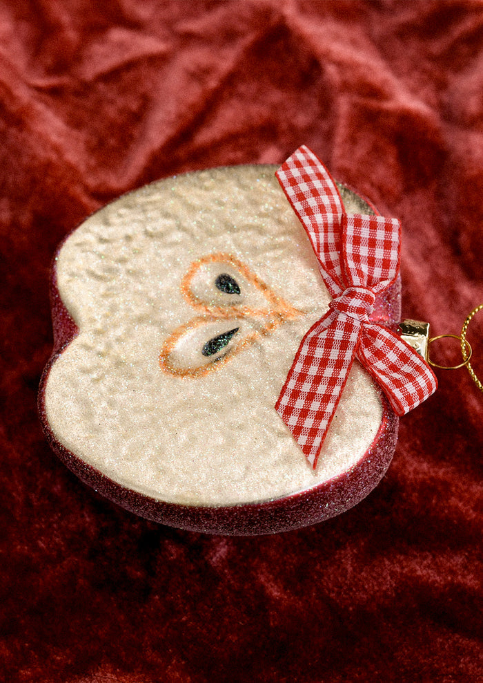 A glass ornament depicting a half apple, decorated with a red gingham bow.