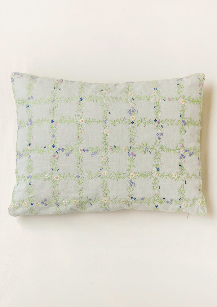 A light blue pillow with an embroidered floral grid pattern.