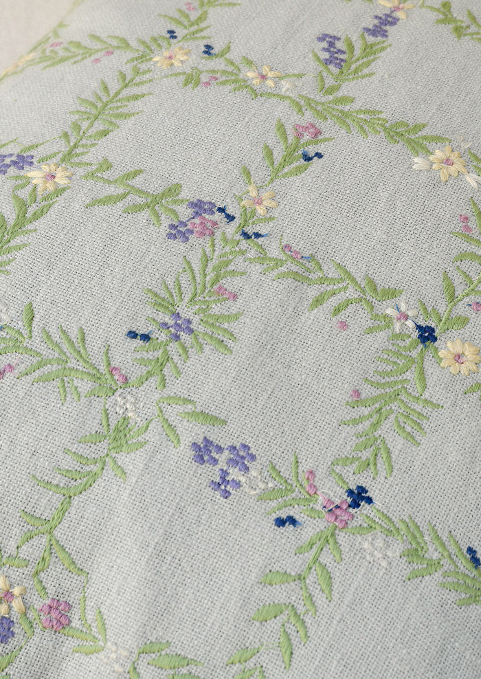 Closeup of a light blue pillow with an embroidered floral grid pattern.
