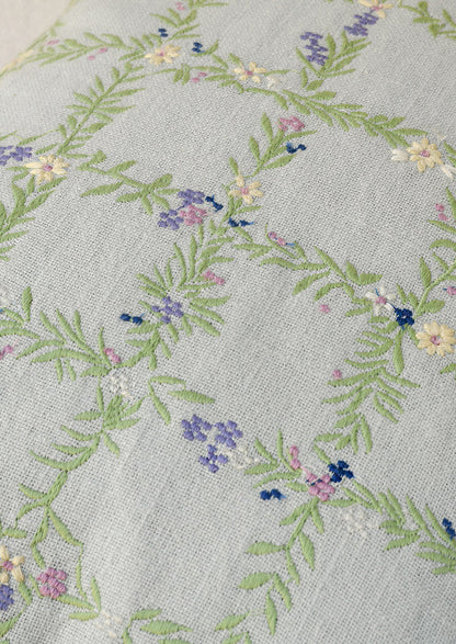 Closeup of a light blue pillow with an embroidered floral grid pattern.