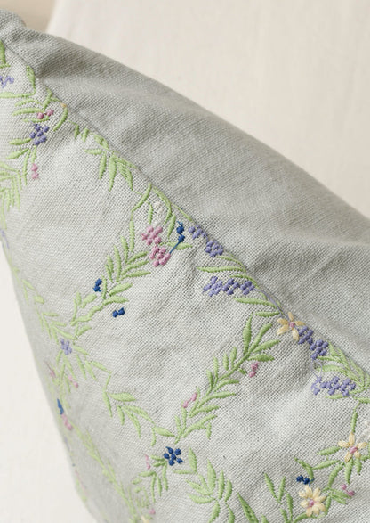 Closeup of a light blue pillow with an embroidered floral grid pattern.