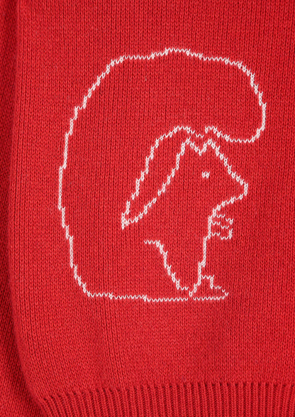 Close-up of a red knit garment featuring a white knitted outline of a squirrel inside a large rounded shape.