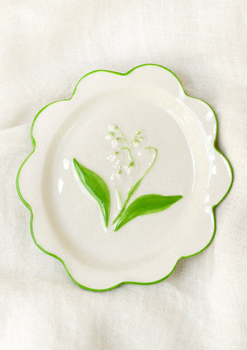 A ceramic plate with scalloped edges and a lily of the valley embossed in the center.