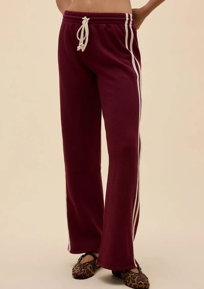 A person wearing burgundy wide-leg sweatpants with white side stripes and a white drawstring, paired with leopard-print flats, against a plain beige background.